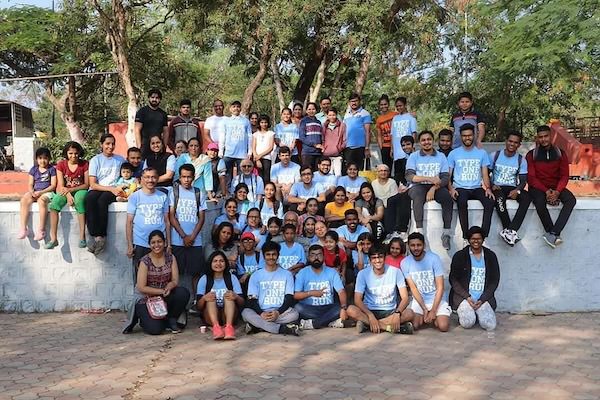 Large group of approximately fifty people in light blue shirts posing together outdoors for a group photo in a park