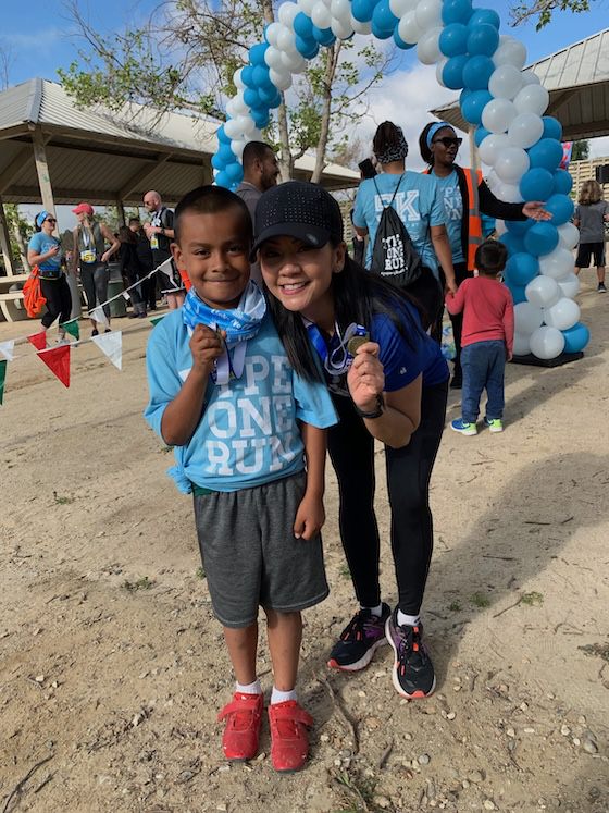 A young boy and a woman smiling proudly while holding finisher medals in front of a balloon arch at an outdoor race event